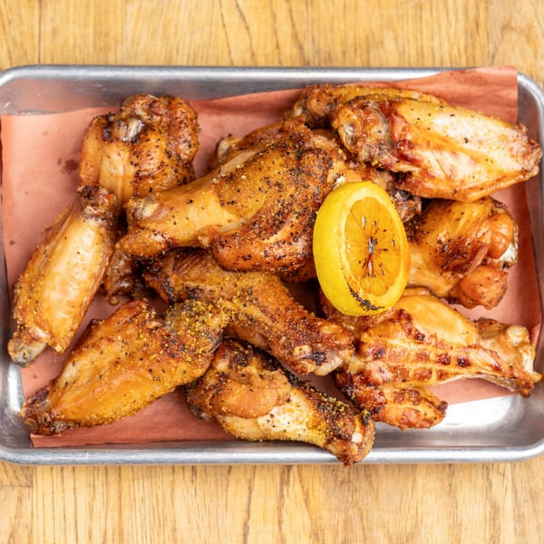 Morgan's Brooklyn Barbecue wings, seasoned and grilled, with a charred lemon wedge on a metal tray.