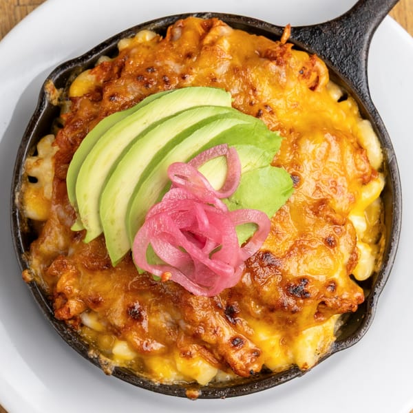 Morgan's Brooklyn Barbecue mac and cheese in a skillet, topped with avocado slices and pickled red onions.