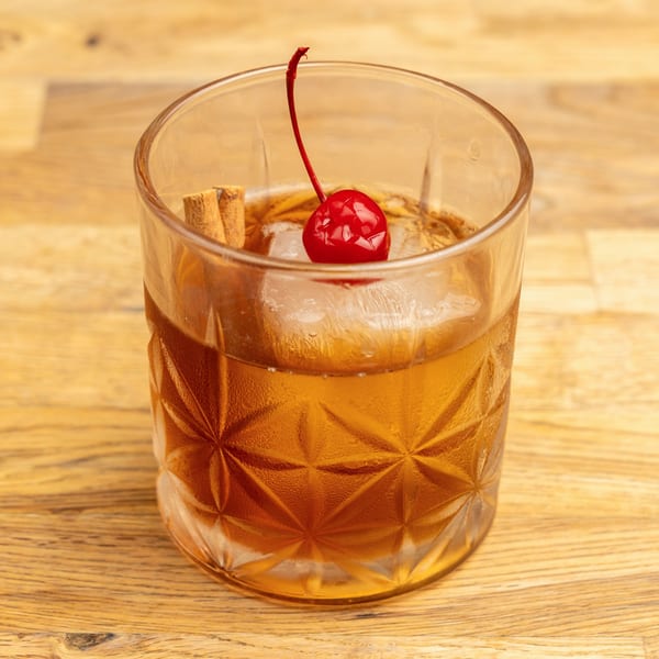 Morgan's Brooklyn Barbecue cocktail with a cherry and cinnamon stick on a wooden table.