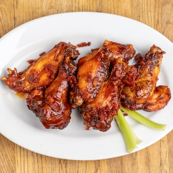 Five BBQ chicken wings with celery sticks on a white plate from Morgan's Brooklyn Barbecue.
