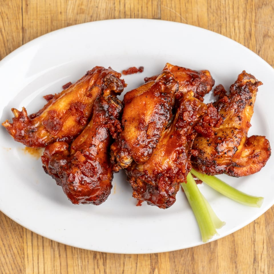 Five BBQ chicken wings with celery sticks on a white plate from Morgan's Brooklyn Barbecue.