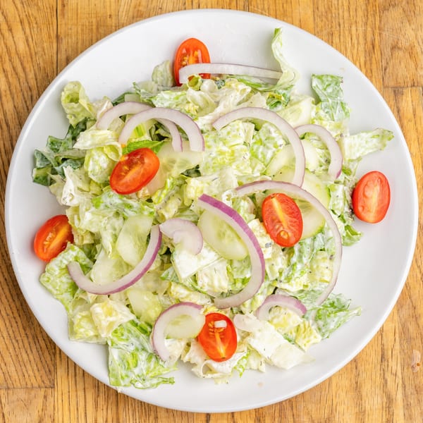 Overhead view of a fresh salad with lettuce, red onions, cucumbers, and cherry tomatoes on a white plate.