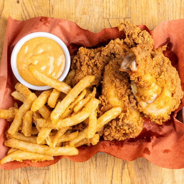 Crispy fried chicken pieces and golden french fries with a side of dipping sauce on a wooden table.