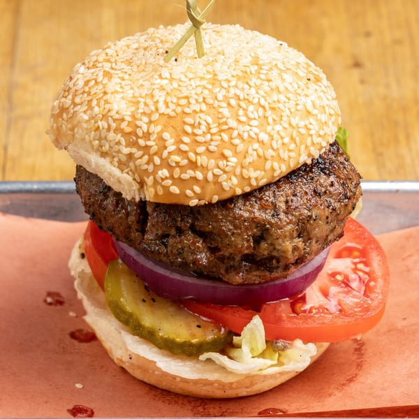 A Morgan's Brooklyn Barbecue burger with a sesame bun, patty, tomato, onion, pickles, and lettuce.