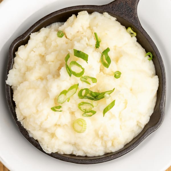 Creamy mashed potatoes topped with fresh green scallions, served in a black cast iron dish.